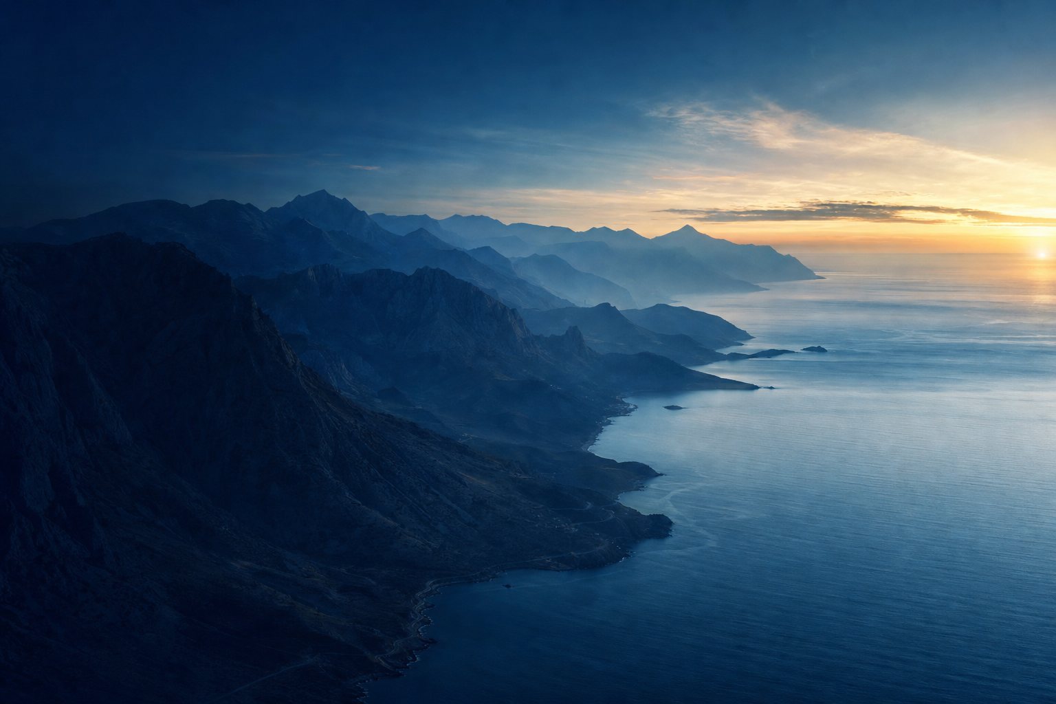 Layered blue mountain ridgelines meeting a calm ocean at dawn